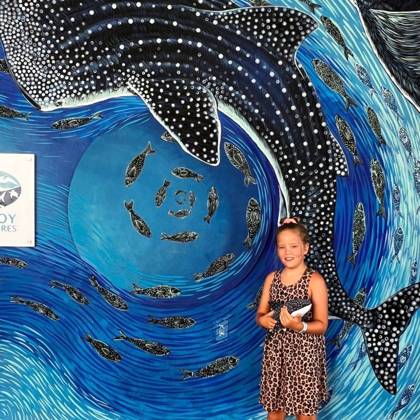 Girl posing in front of a whale shark with her plushie